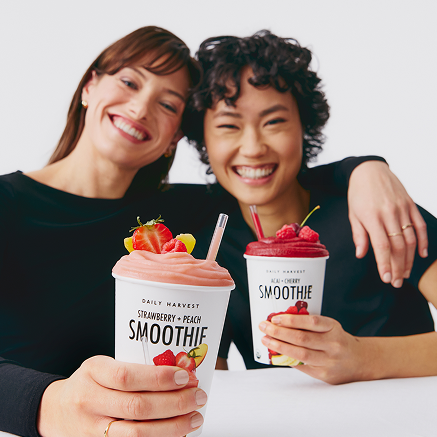 two women smiling with two smoothies.