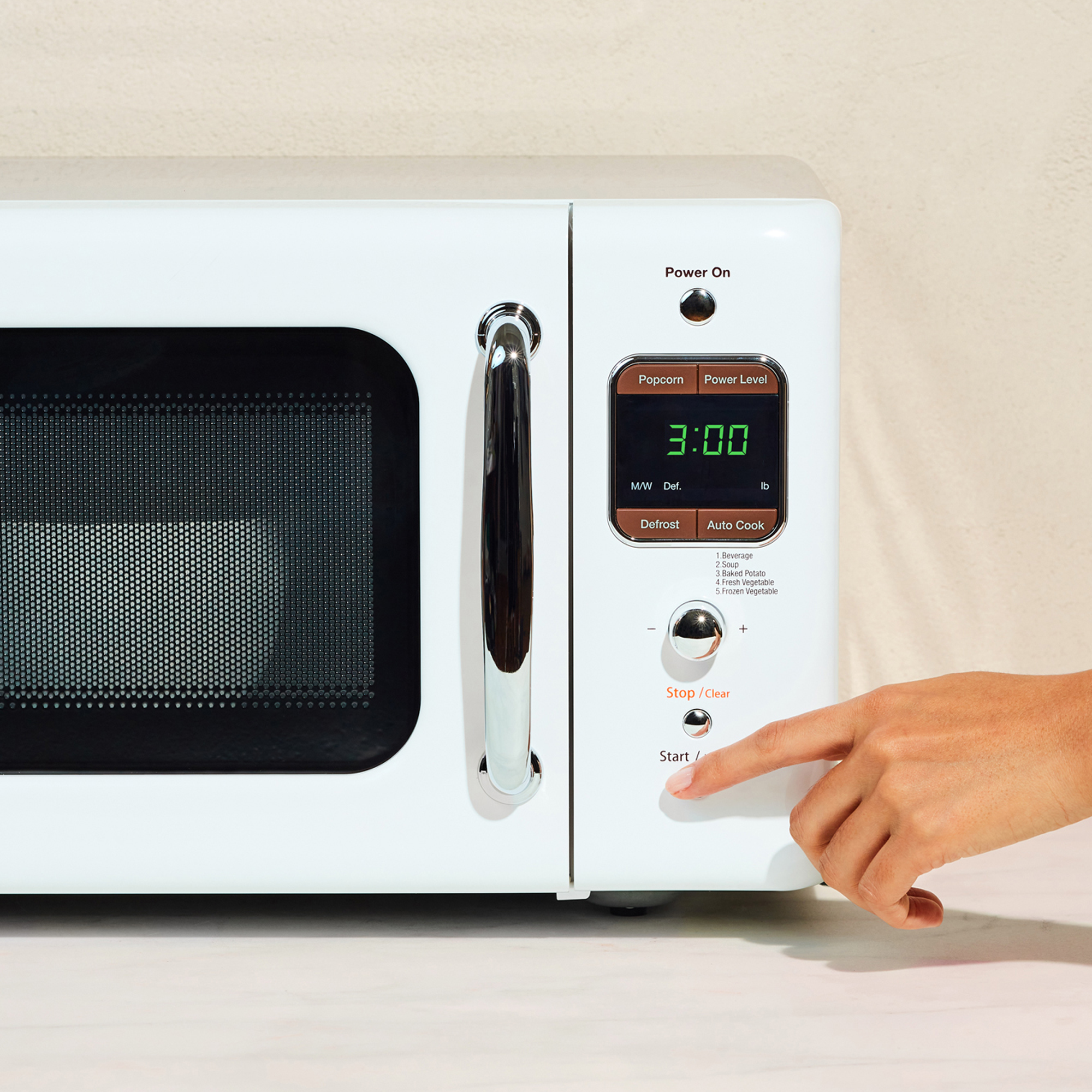 Hand pressing a button on a white microwave oven with a digital display.