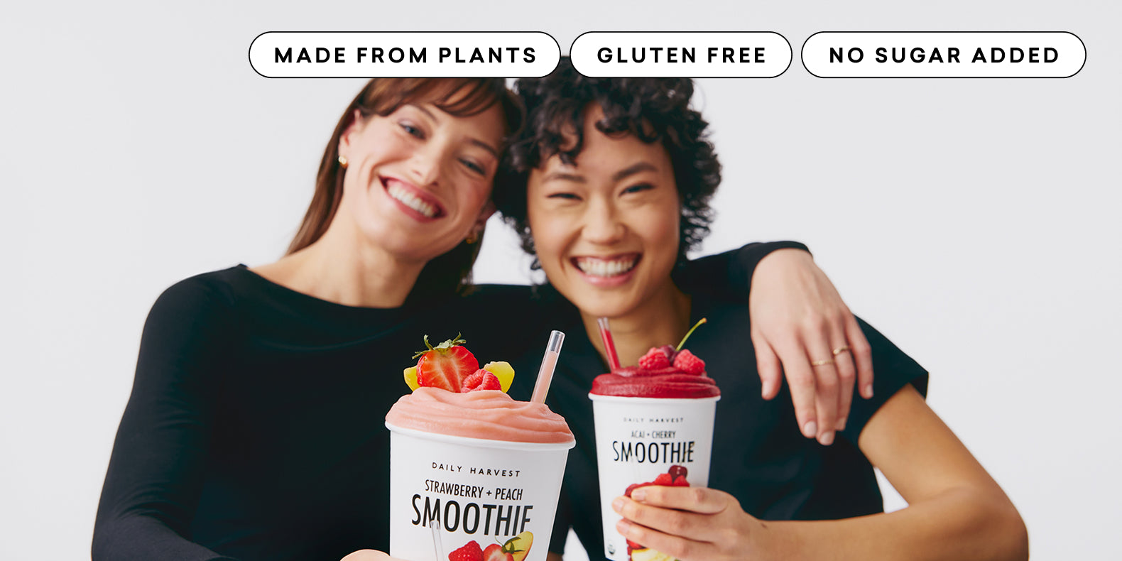 Two people holding smoothie cups with text indicating 'No Added Sugar', 'Gluten-Free', and 'Made from Plants'.
