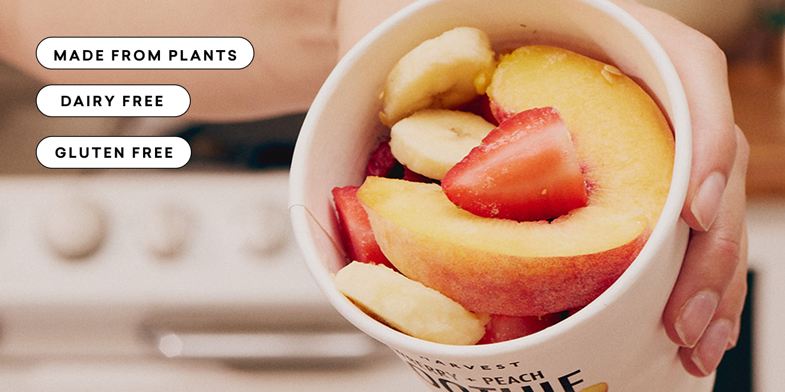Hand holding a cup filled with fresh sliced peaches, strawberries, and bananas with dietary labels nearby