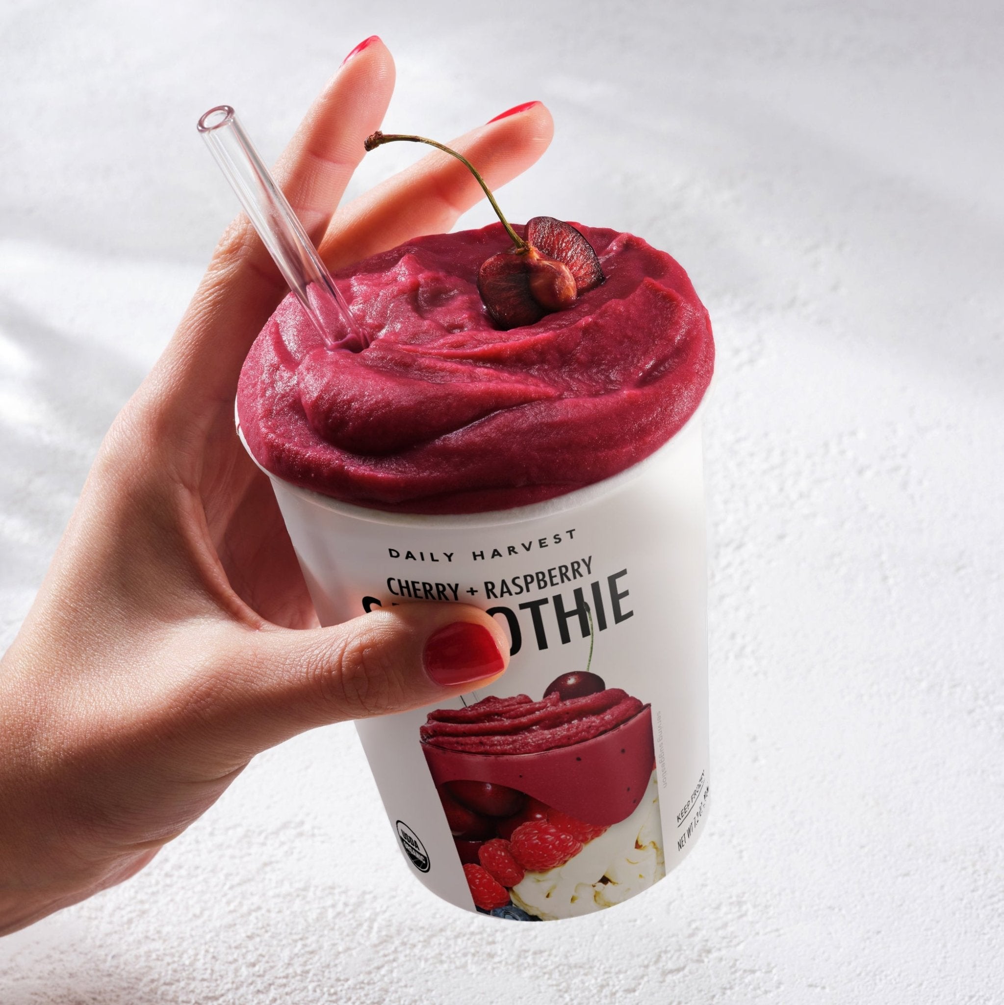 Hand holding a cup filled with thick cherry raspberry smoothie topped with fresh cherries and a straw