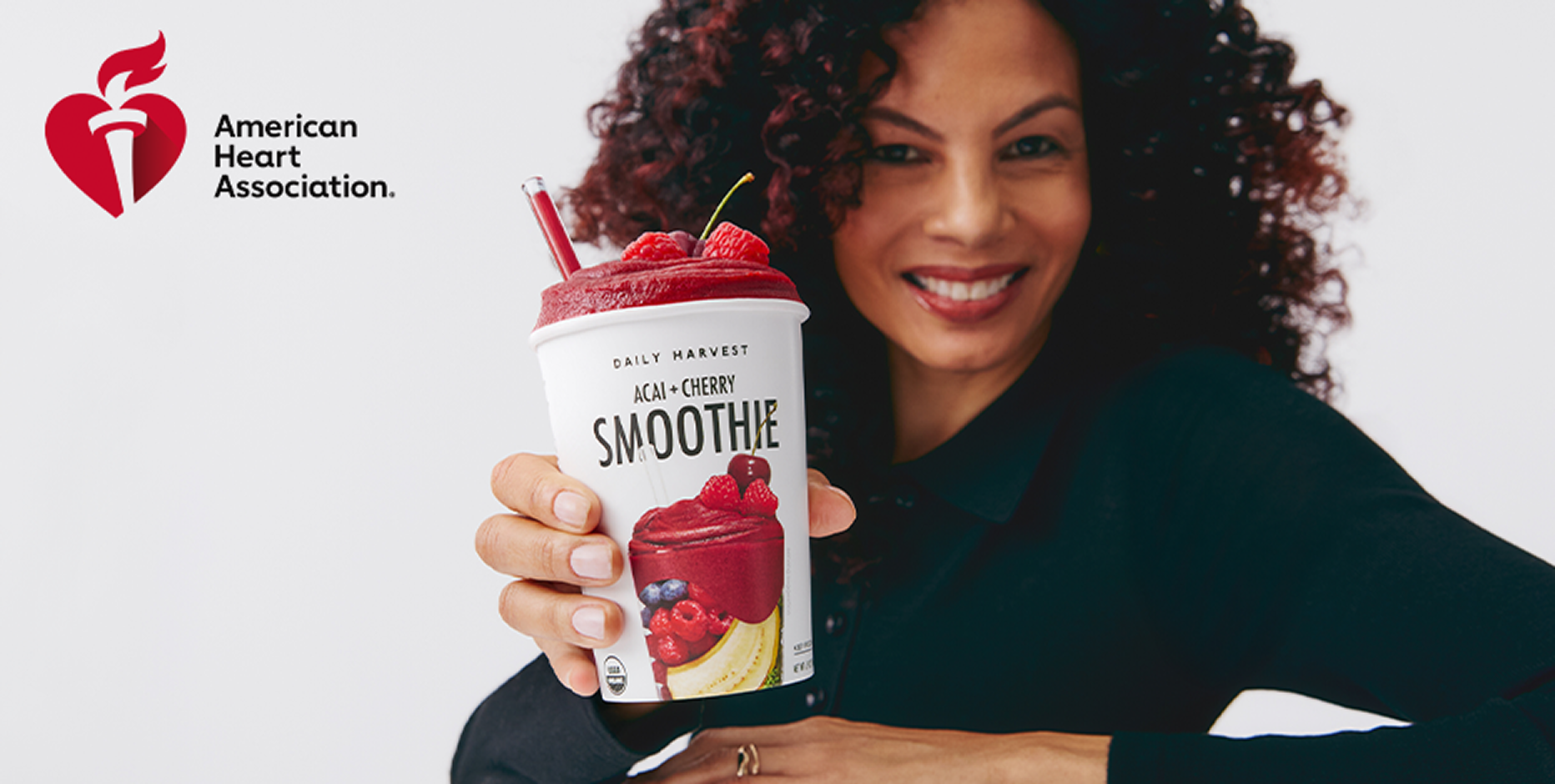 Woman holding a healthy acai cherry smoothie cup with American Heart Association logo on white background