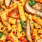 Top-down view of a colorful pasta dish with noodles, vegetables, and herbs on a black plate on a wooden surface