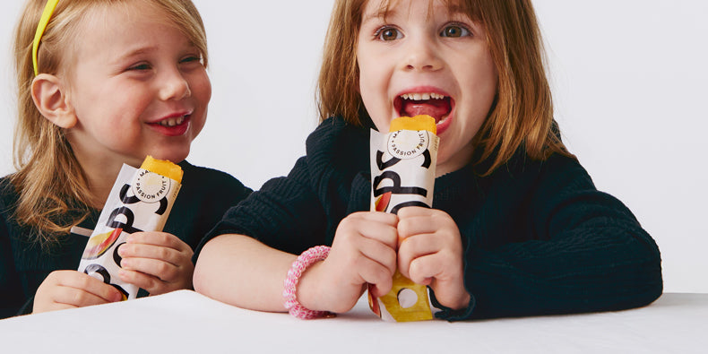 Two children smiling and eating Mango + Passion Fruit Pops