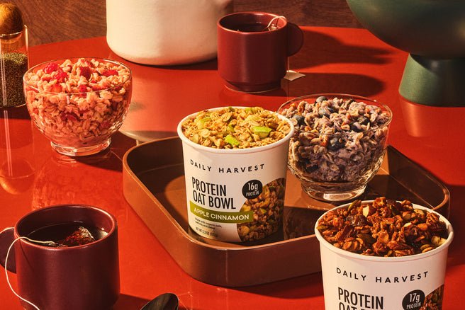 Daily Harvest protein oat bowls on a red table with teacups and fruit.