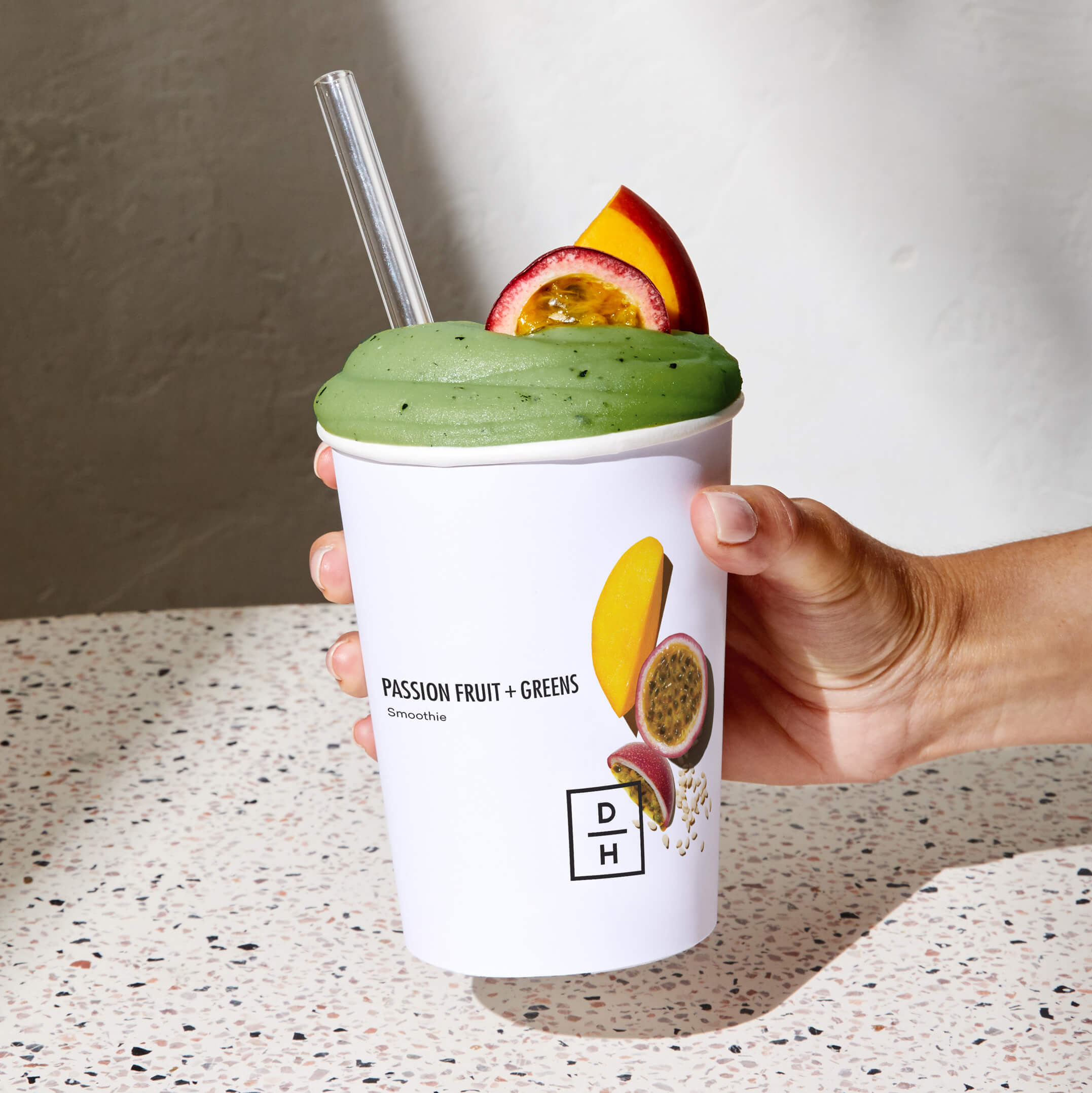 A hand holding a prepared Passion Fruit + Greens Smoothie 