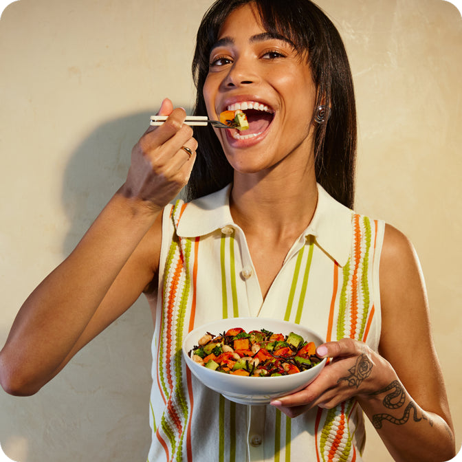 A woman eating a Sweet Potato + Wild Rice Hash Bowl with a fork.