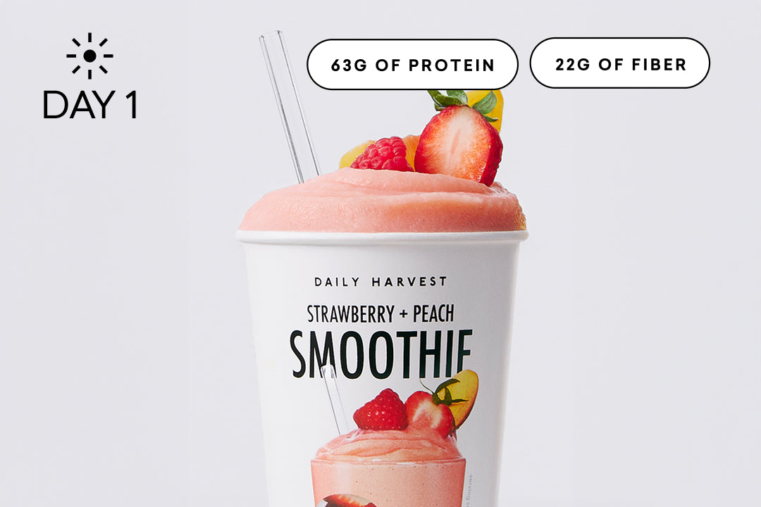 Close-up of a purple smoothie topped with a strawberry slice and blueberries in a Daily Harvest cup with straw