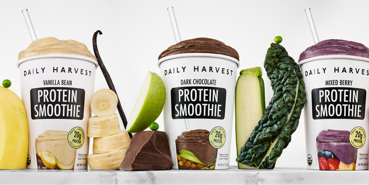 Three Daily Harvest protein smoothies with mixed berry, vanilla bean, and dark chocolate flavors with fresh ingredients displayed