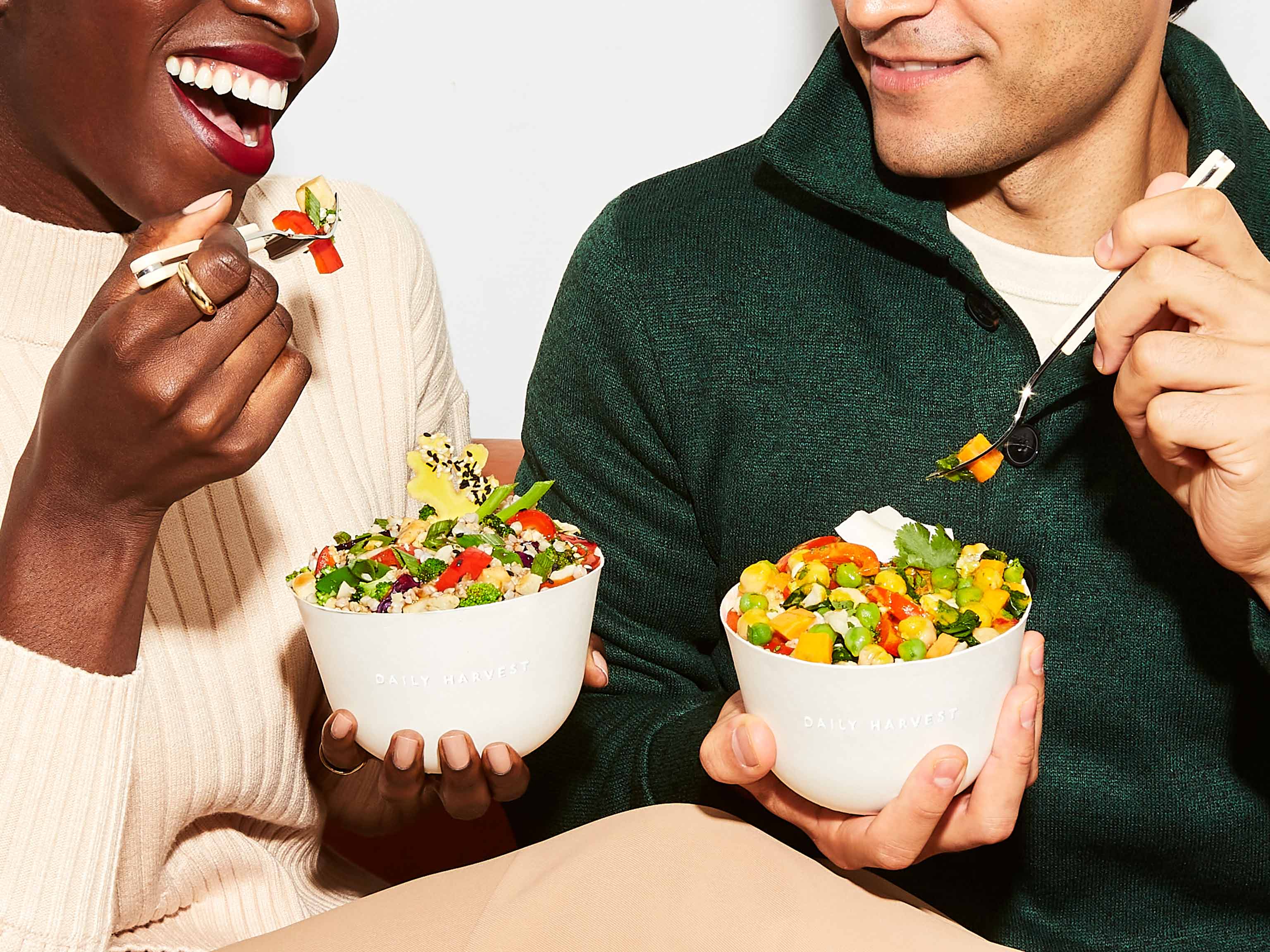 Two people eating harvest bowls with forks. 