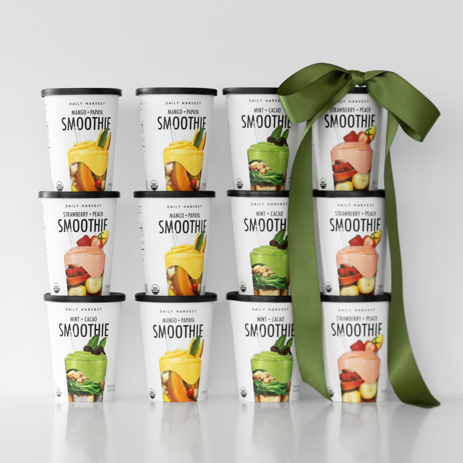 Twelve assorted Daily Harvest best-selling smoothies stacked with a green bow and sale sign on white background