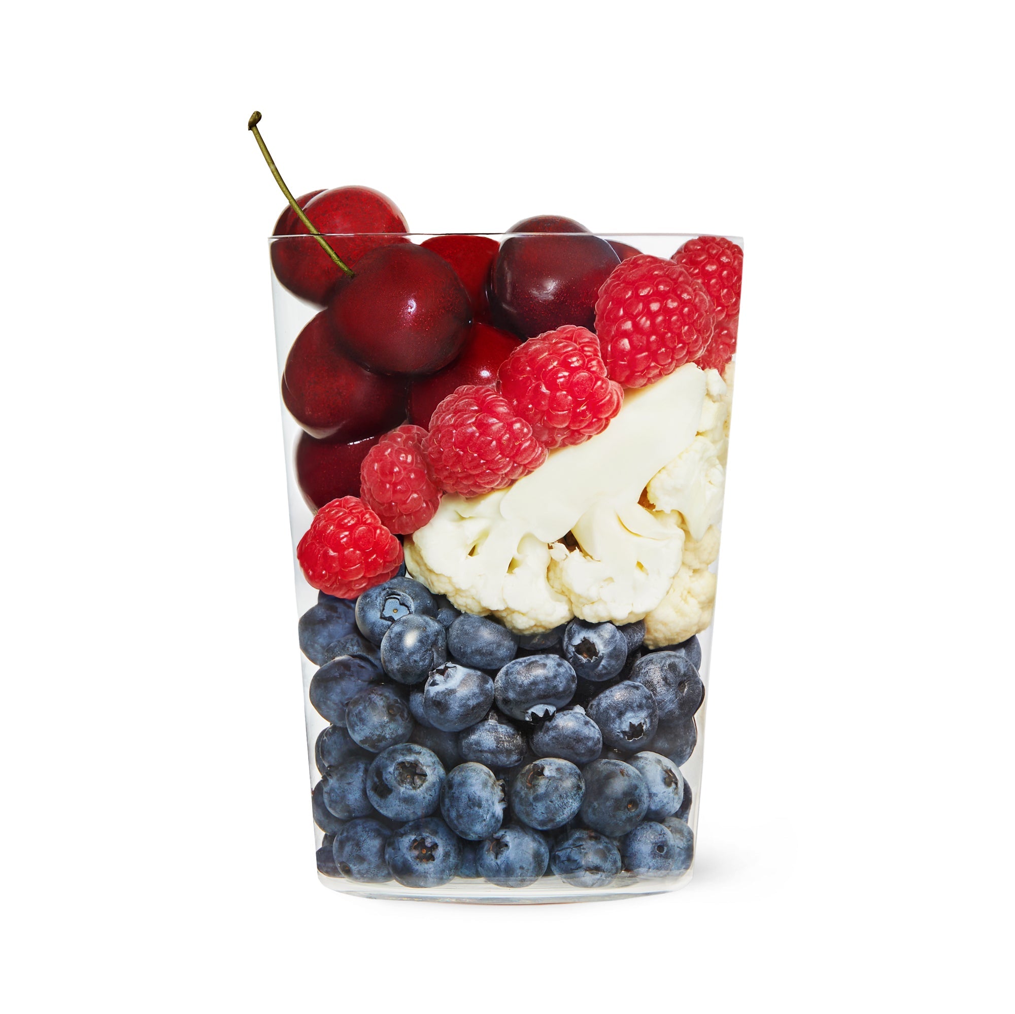 Clear cup filled with layered blueberries, cauliflower, raspberries, and cherries on a white background