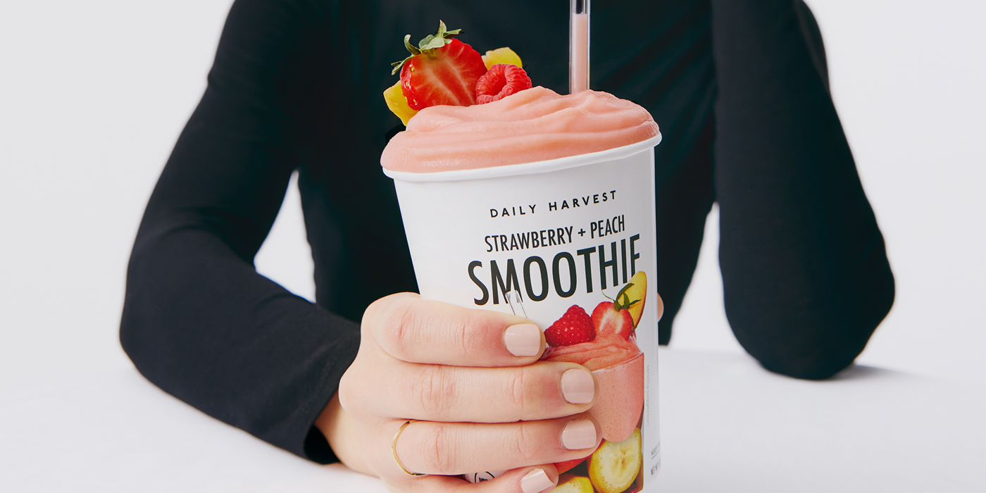 Person holding a Daily Harvest strawberry peach smoothie with visible branding.
