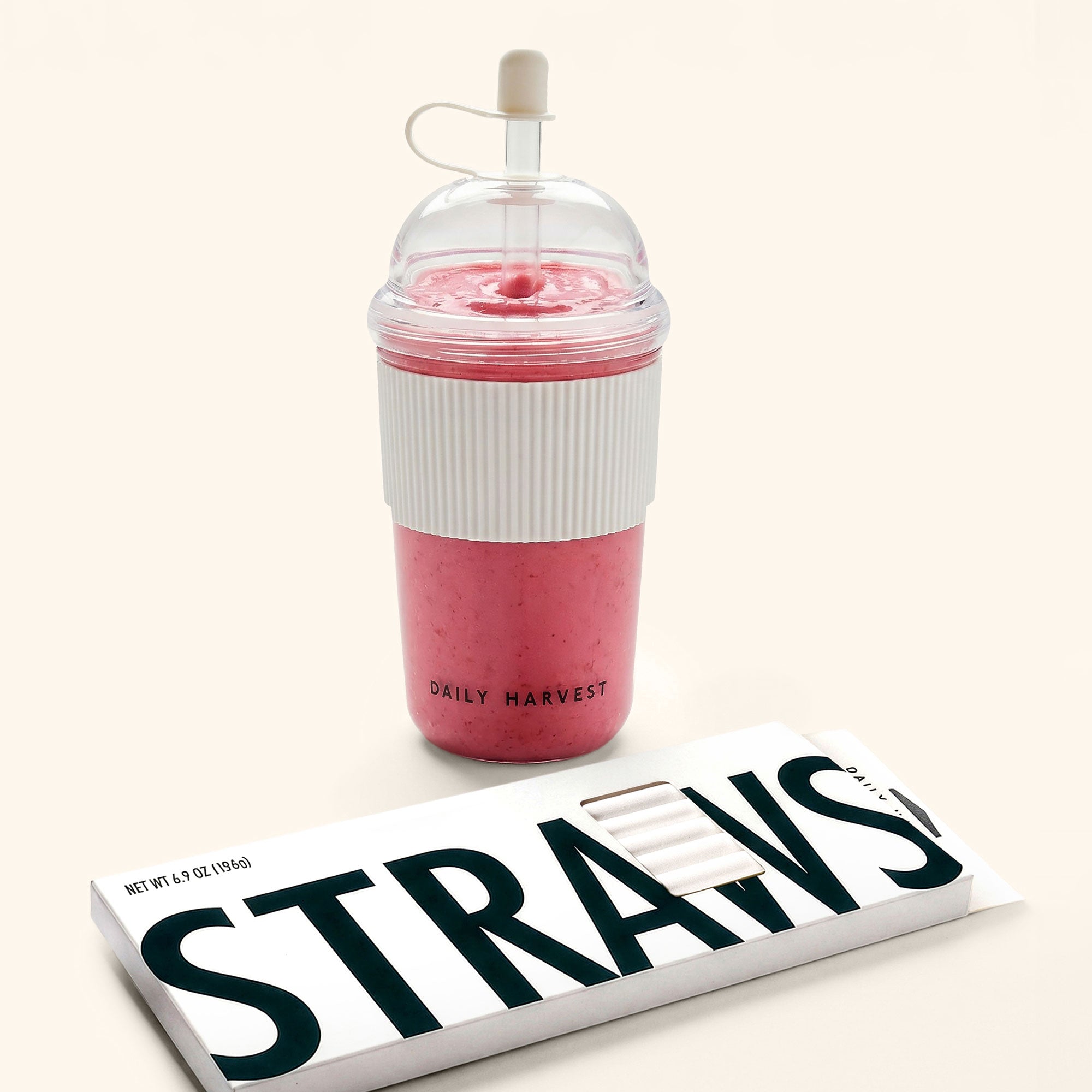 Pink smoothie in a clear cup with a straw, placed on a white surface.